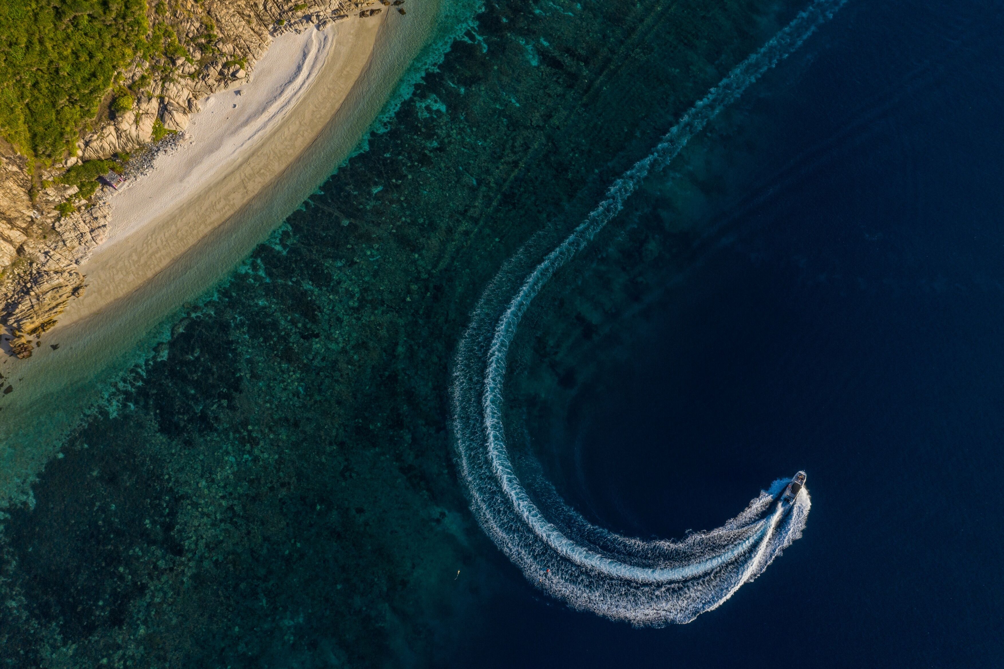 An aerial view of a beach with a boat creating a wake in the water.