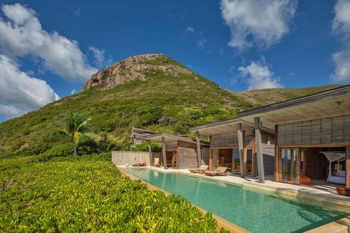 A modern resort with a pool, lounge chairs, and a mountain backdrop.