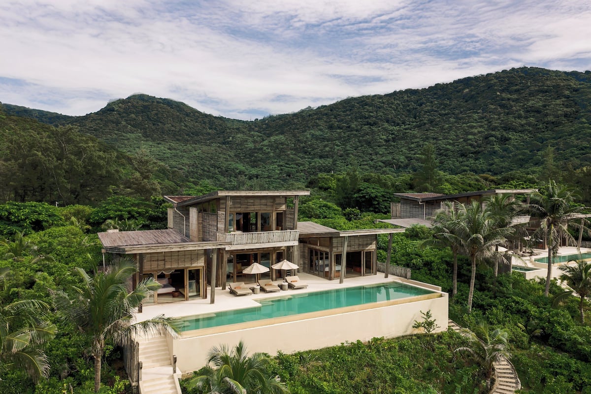 A two-story house with a swimming pool, surrounded by lush greenery and hills.
