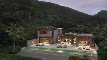 A modern two-story house with a swimming pool, surrounded by lush greenery and hills.