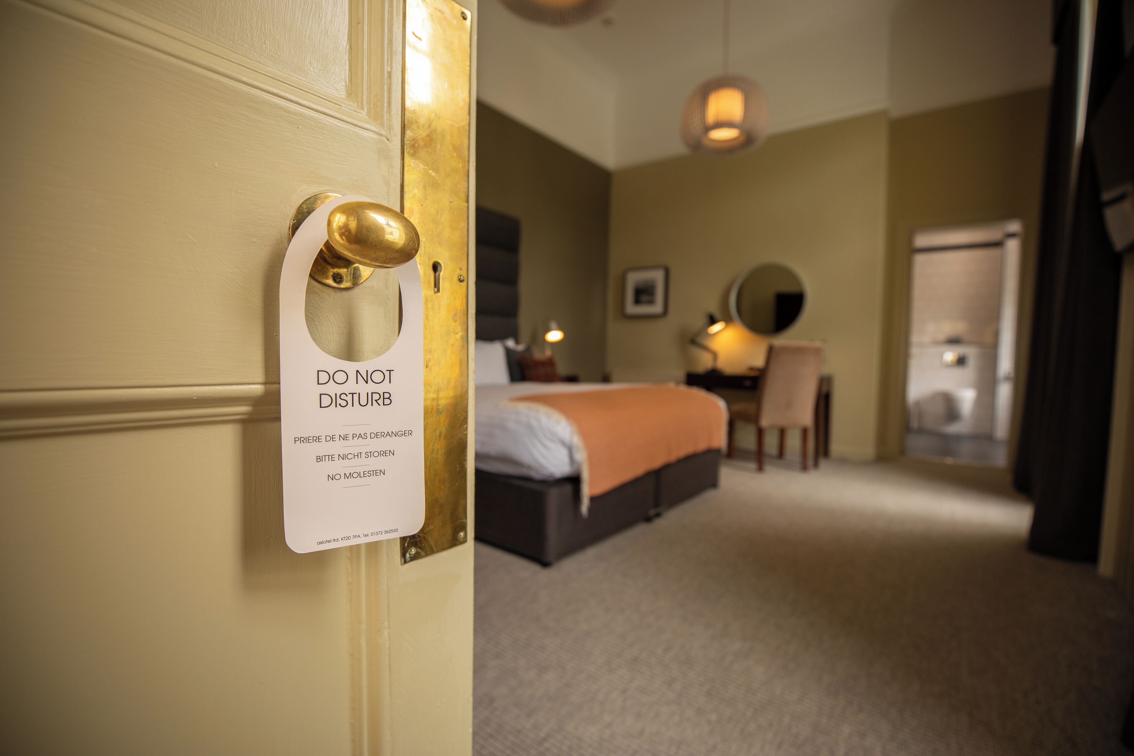 A hotel room with a bed, a desk, and a chair. There is a sign on the door that says 'DO NOT DISTURB'.