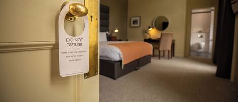 A hotel room with a bed, a desk, and a chair. There is a sign on the door that says 'DO NOT DISTURB'.