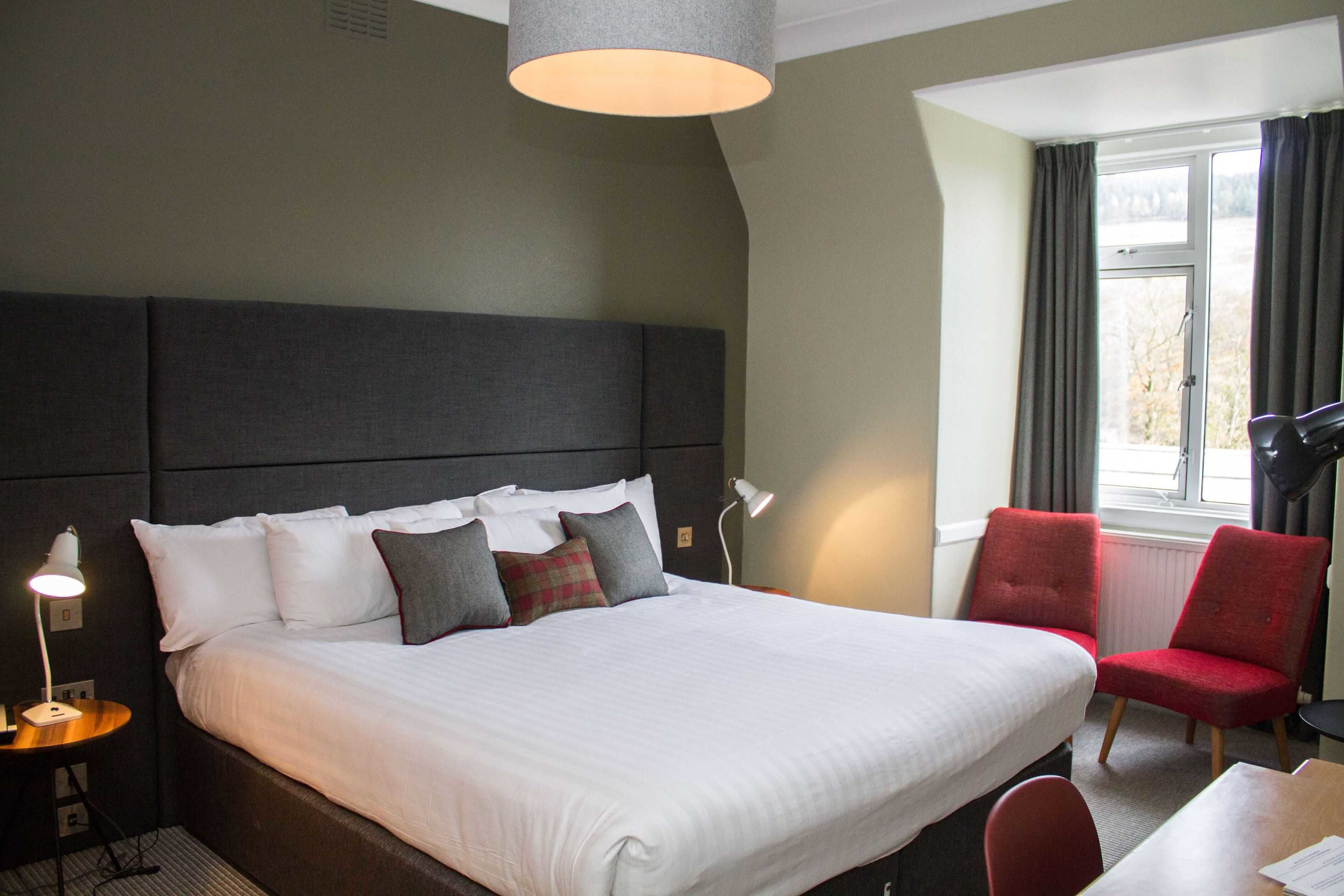 A hotel room with a large bed, a desk, a chair, and a window with curtains.