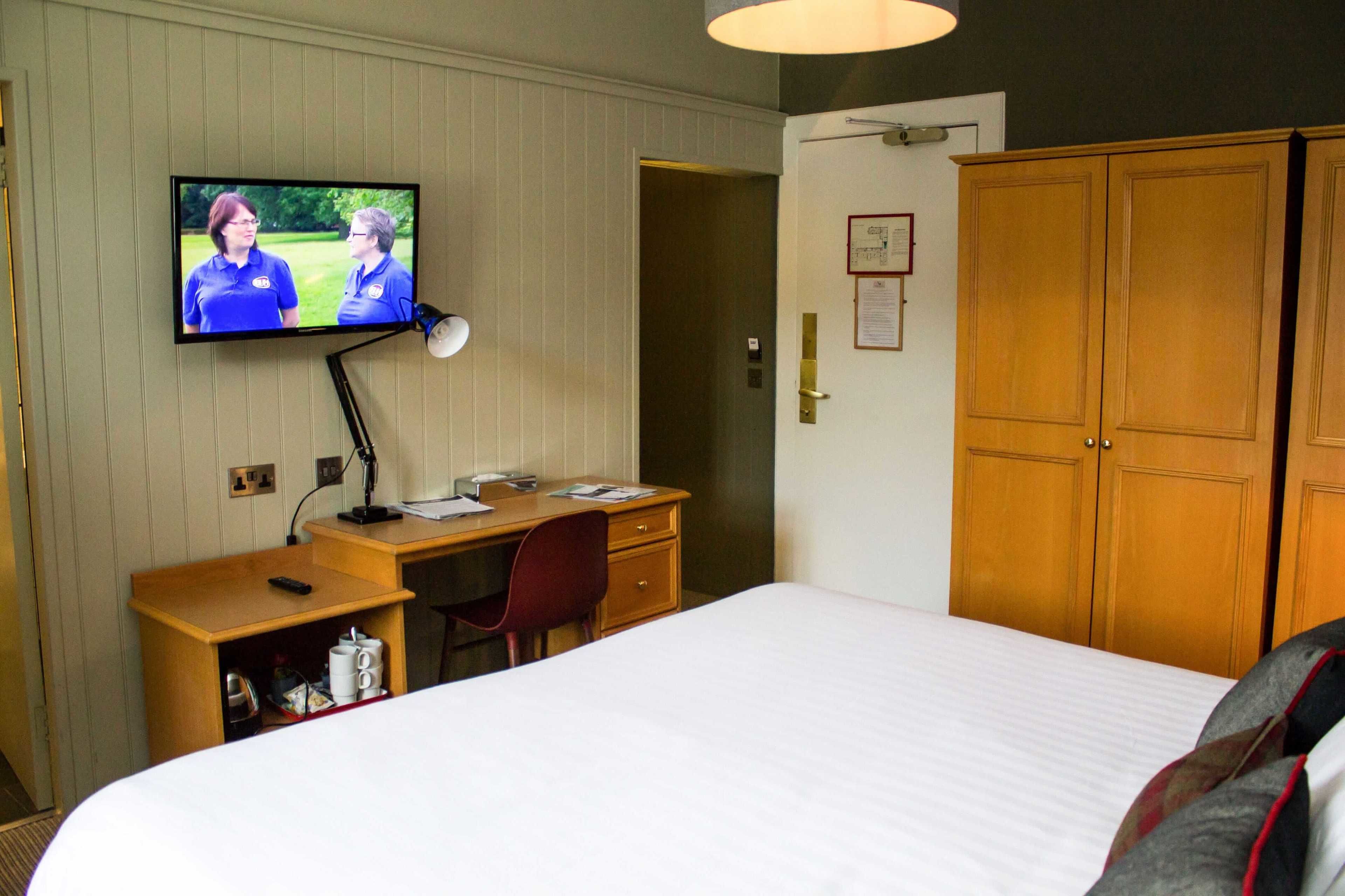 Una habitación de hotel con cama, escritorio, silla, televisor, armario y puerta.