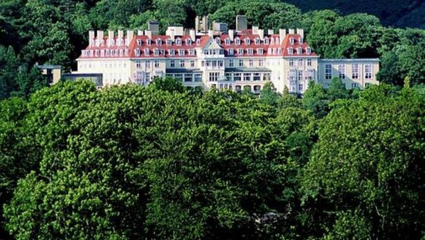 A large, multi-story building with a red roof, surrounded by lush green hills and dense forest.