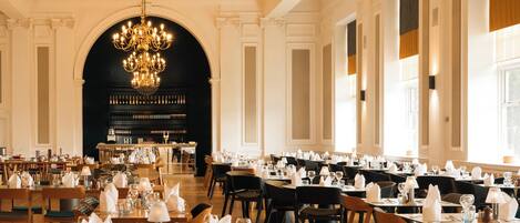 Un comedor formal con mesas dispuestas para el servicio, una araña y una estantería para vinos al fondo.