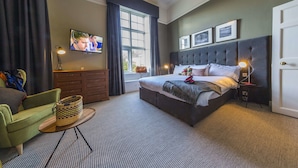 A modern hotel room with a large bed, a television, a desk with a lamp, and a view of the outdoors through a window.
