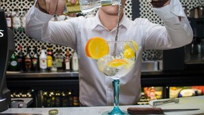 A bartender pouring a drink into a glass with ice and orange slices.
