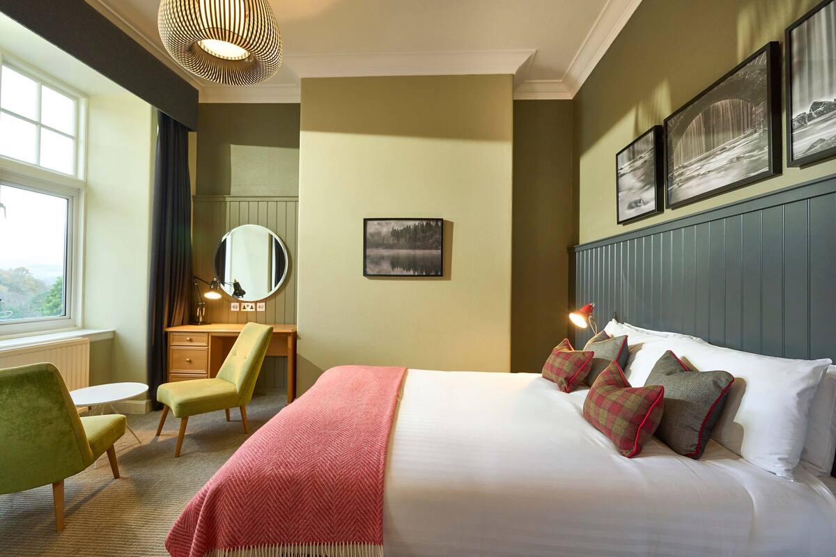 A hotel room with a bed, a desk, a chair, a mirror, and artwork on the walls.