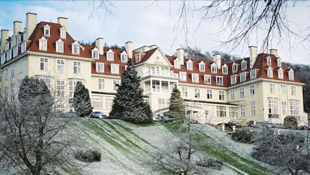 A large, multi-story building with a symmetrical facade, multiple chimneys, and a sloped roof.