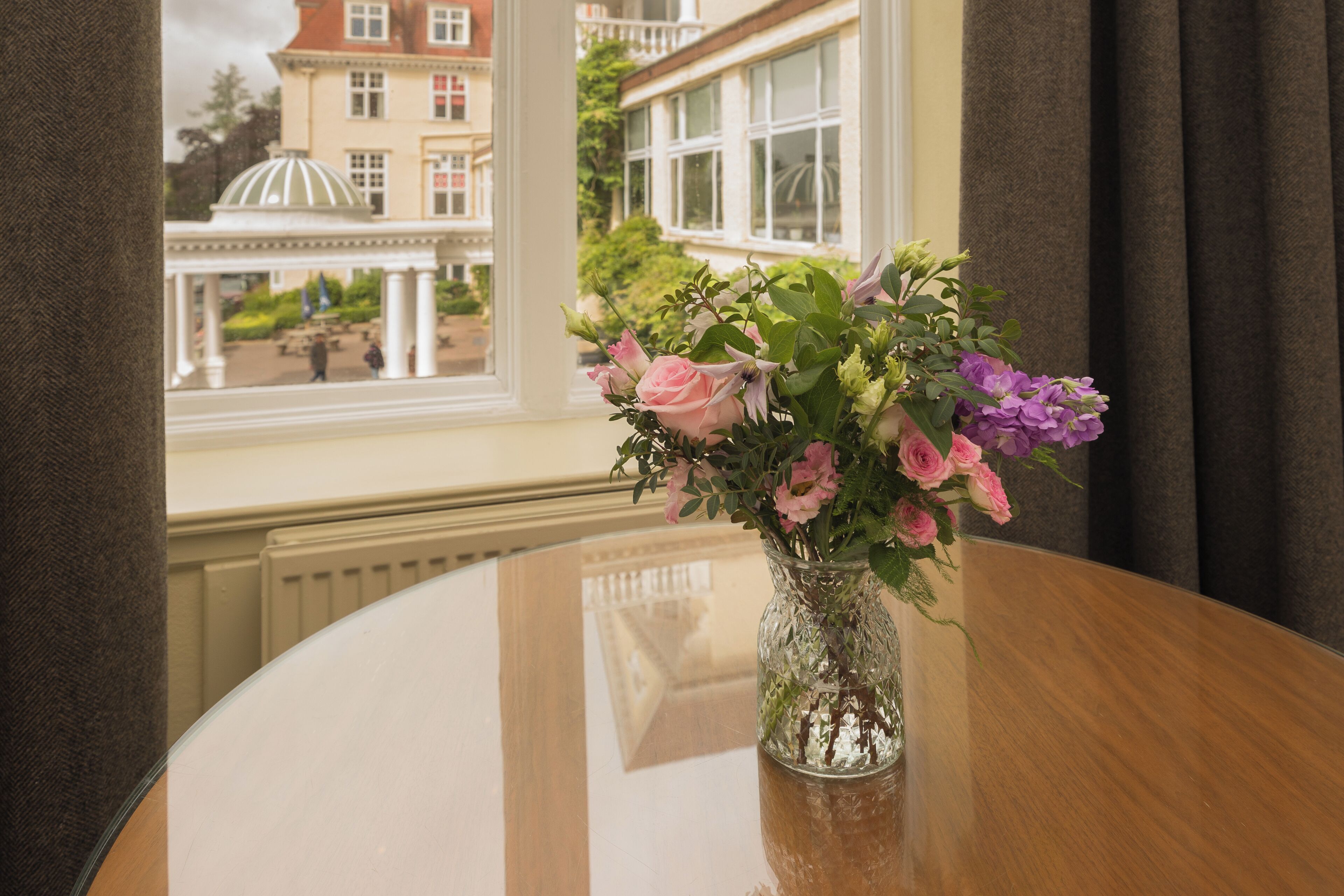 A round table with a glass vase containing pink and purple flowers.