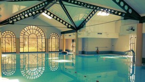 An indoor swimming pool with arched windows, a diving board, and a lifeguard chair.