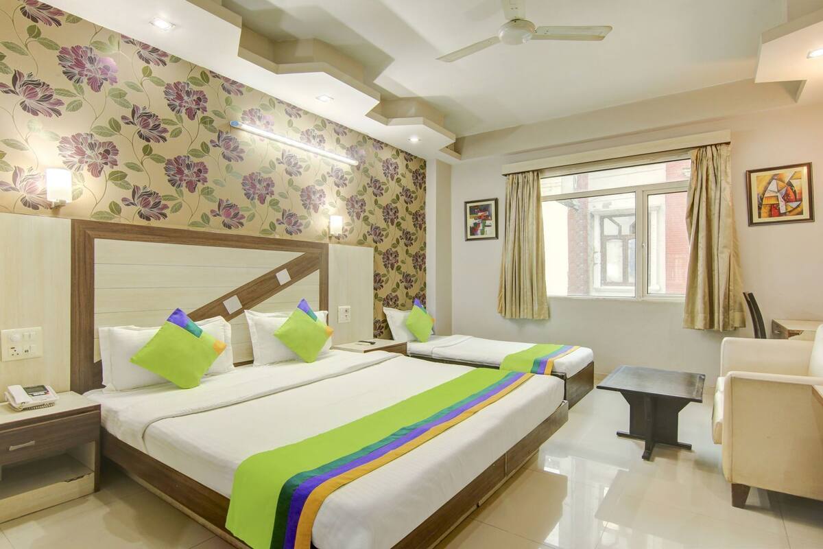 A hotel room with two beds, a desk, a chair, a window with curtains, and a ceiling fan.