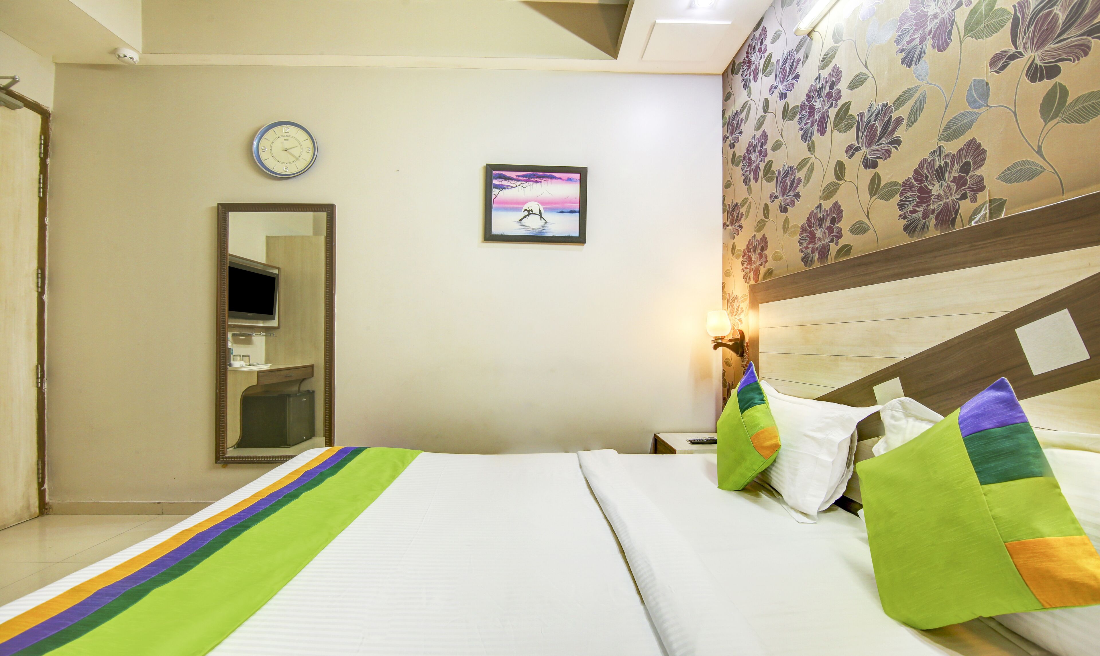 Habitación de hotel con una cama, un reloj, un cuadro enmarco y un papel tapiz floral.