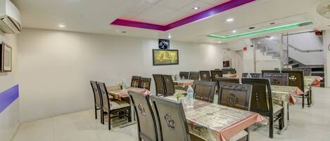 A dining area with multiple tables and chairs, a framed picture on the wall, and a staircase in the background.