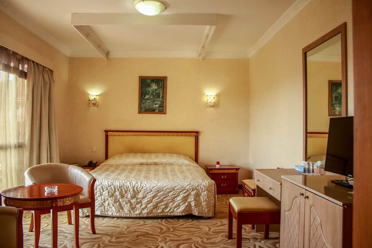 A hotel room with a large bed, a desk, a chair, a small table, and a television.
