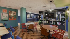 A modern interior with wooden flooring, a bar area, and a bookshelf with plants. - Travelodge Edinburgh Cameron Toll (Edinburgh)