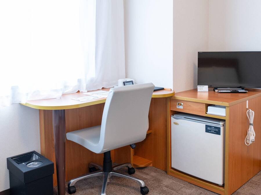 Ein Hotelzimmer mit Schreibtisch, Stuhl, Fernseher, Minikühlschrank und Mülleimer.