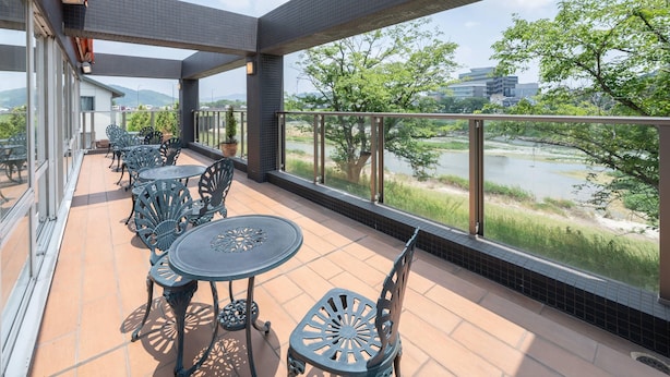 A covered outdoor area with multiple tables and chairs, overlooking a river and greenery.
