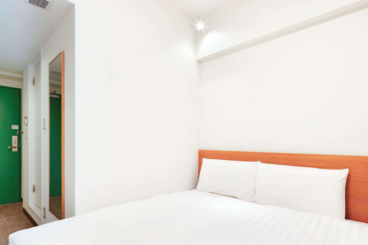 A hotel room with a large bed, a wooden headboard, and a green door.