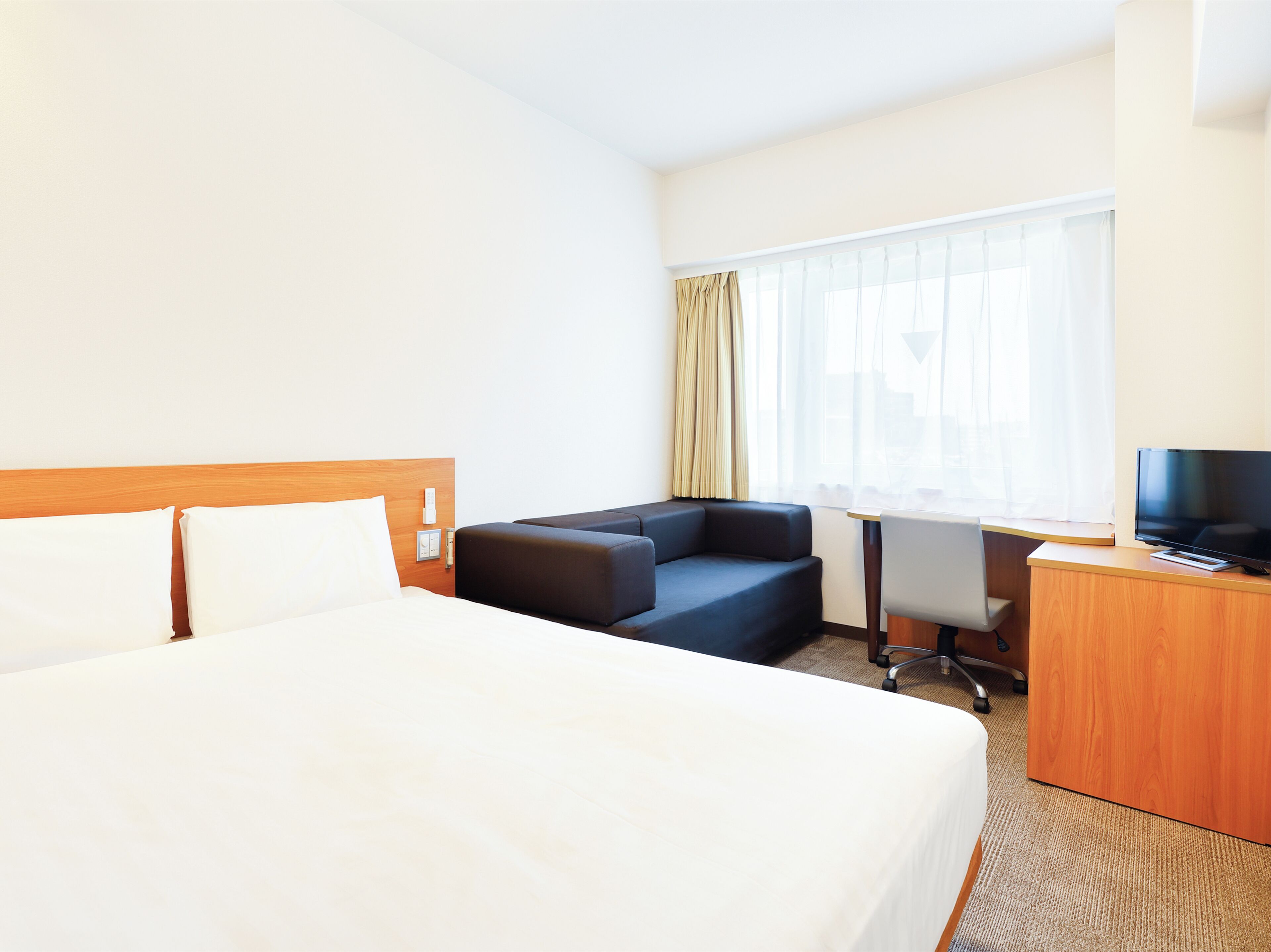 Une chambre d’hôtel avec un grand lit, un bureau, une chaise, une télévision et une fenêtre avec des rideaux.