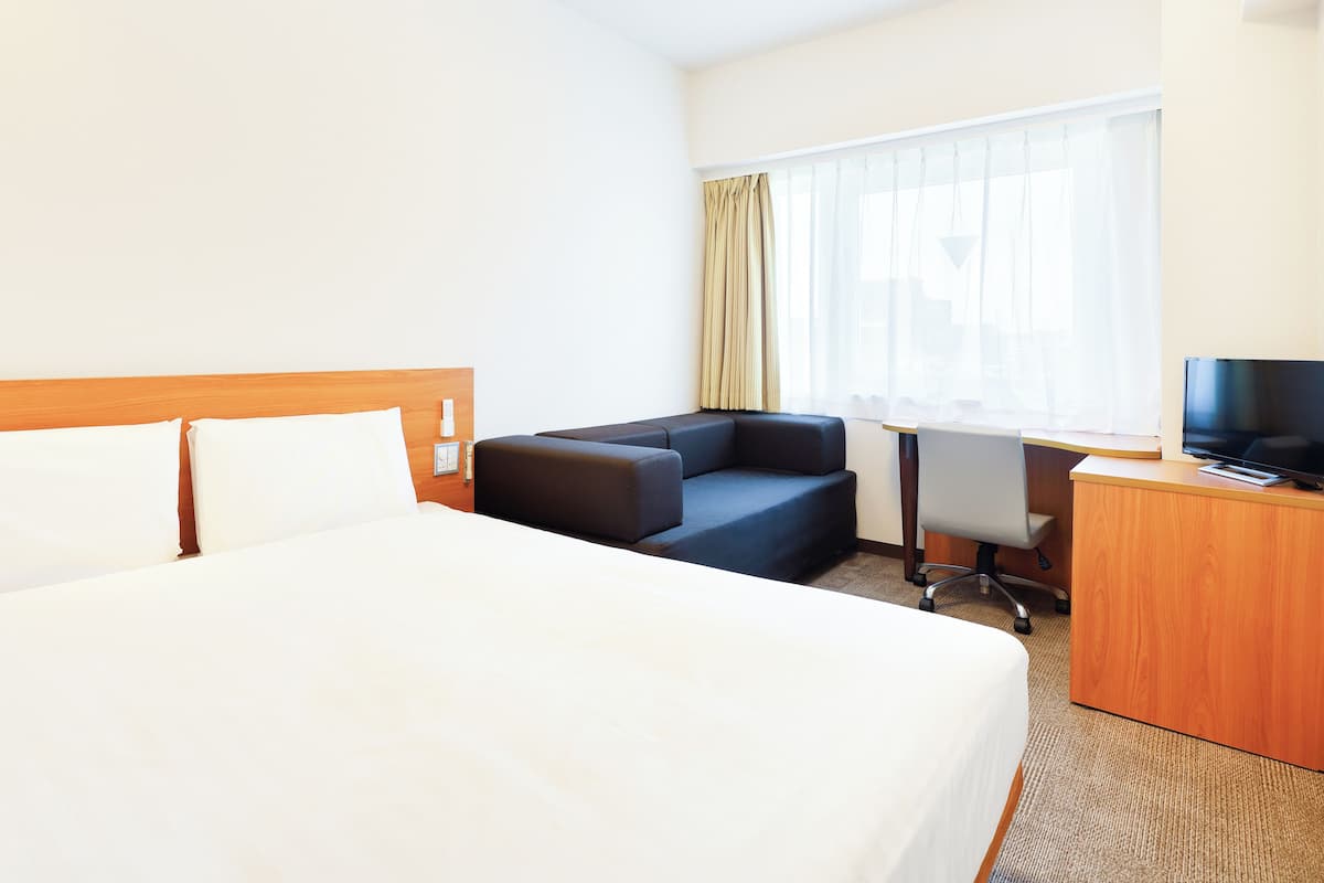 A hotel room with a large bed, a desk, a chair, a TV, and a window with curtains.