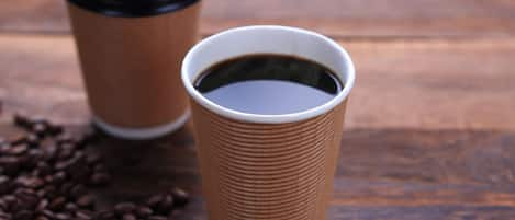 Two paper coffee cups with lids on a wooden surface, surrounded by coffee beans.