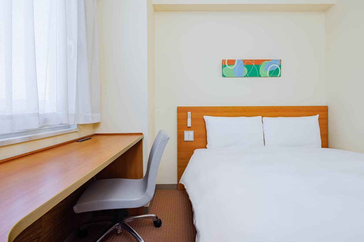 A hotel room with a bed, a desk, a chair, and a window with curtains.