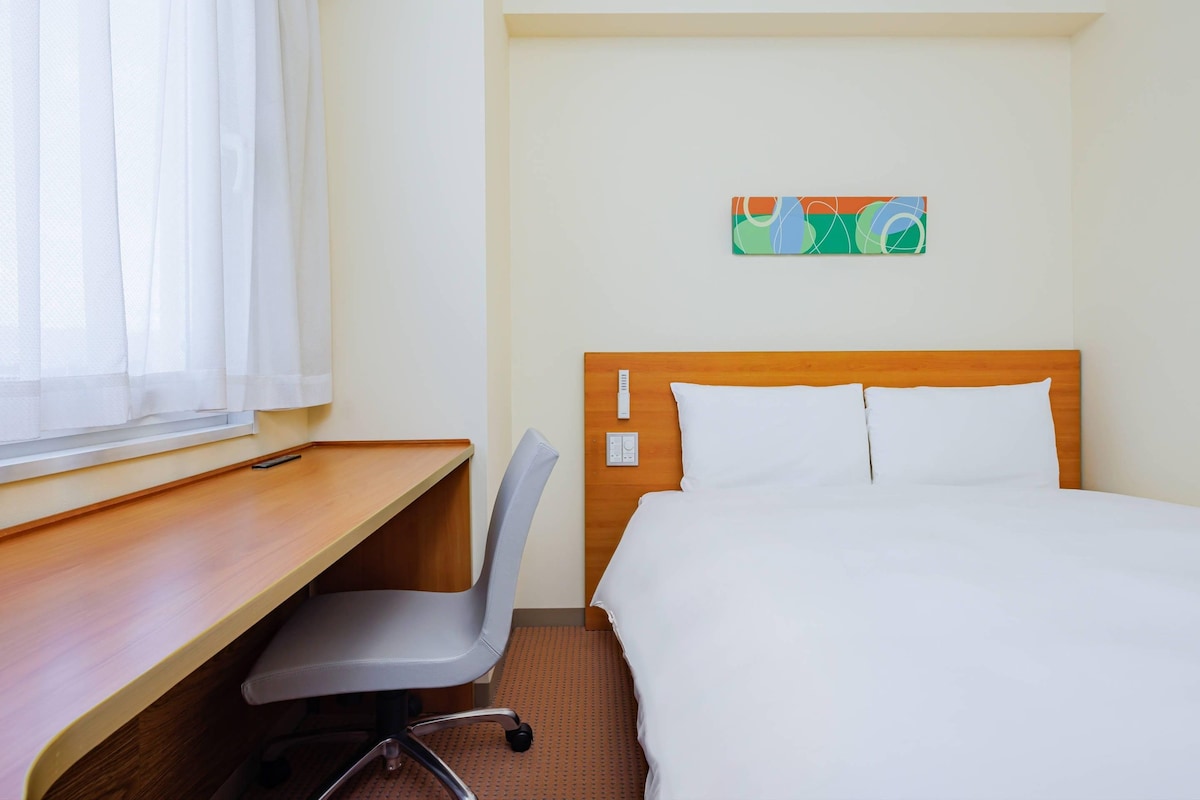 A hotel room with a bed, a desk, a chair, and a window with curtains.