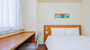 A hotel room with a bed, a desk, a chair, and a window with curtains.
