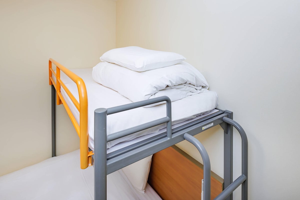A bunk bed with a wooden lower bunk and an orange upper bunk.