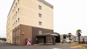 Un hôtel à plusieurs étages, doté d’une façade sobre, d’une entrée abritée et d’un parking où sont stationnées plusieurs voitures.