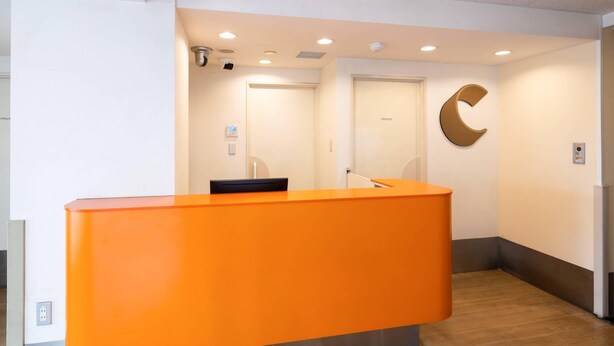 Un espace d’accueil avec un bureau orange vif, une horloge murale et une porte donnant accès à un espace privé.