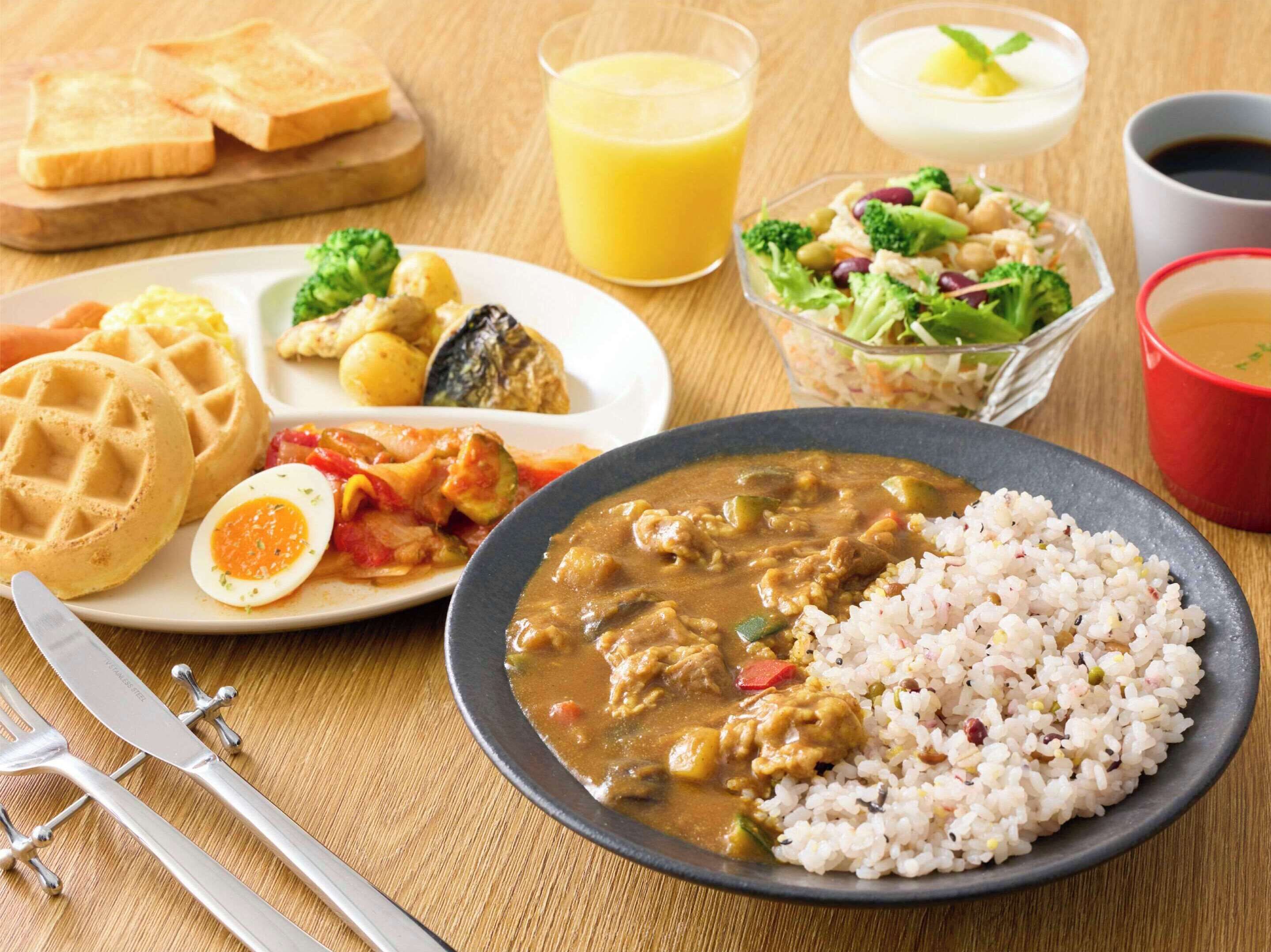 Eine Mahlzeit mit Reis, einem Currygericht, Toast, Salat und einem Glas Orangensaft.