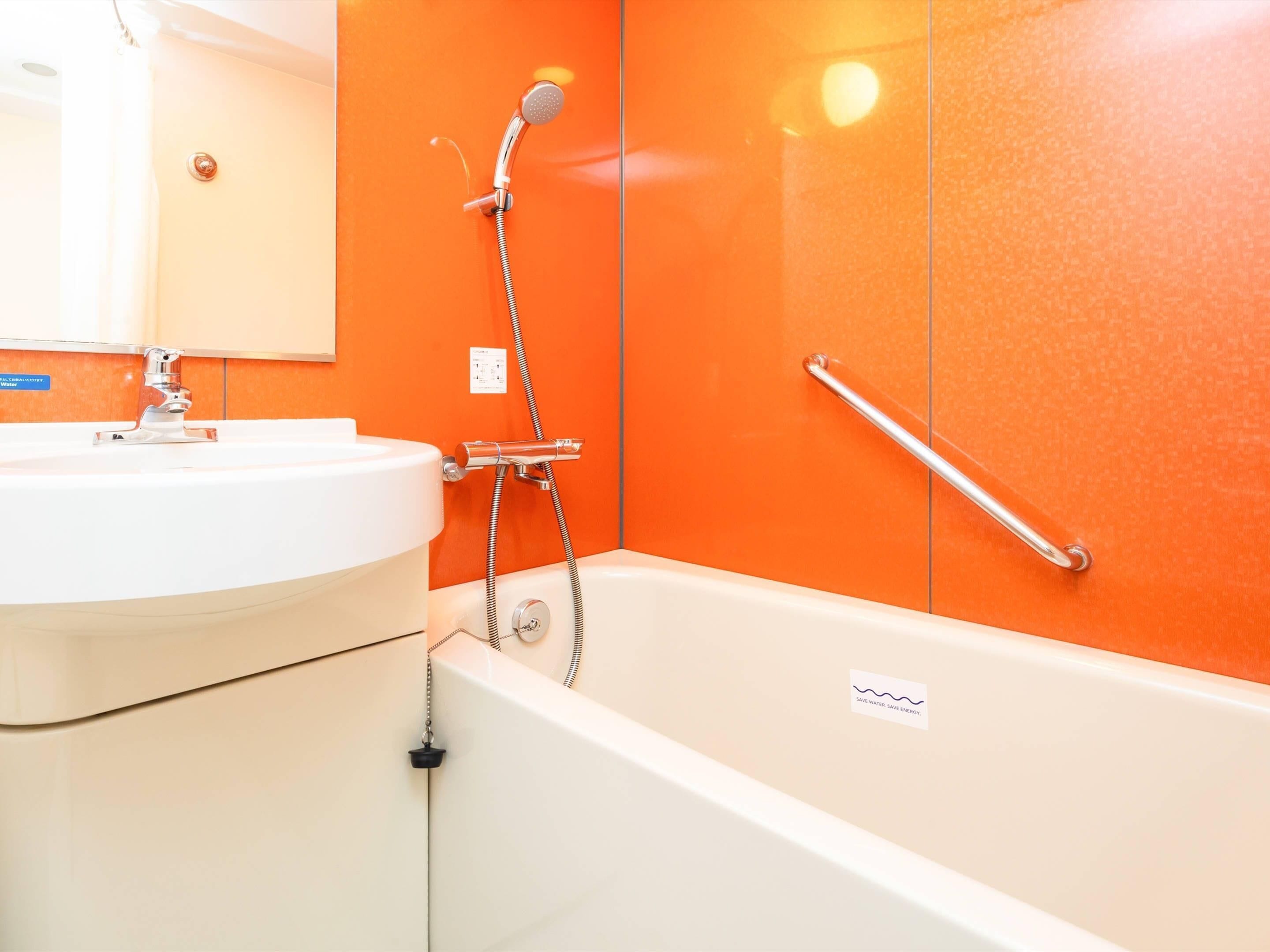 Ein Badezimmer mit einem weißen Waschbecken, einer Badewanne und einer orangefarbenen Wand.