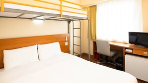 Une chambre d’hôtel équipée d’un lit superposé, d’un bureau avec un ordinateur, d’une télévision et d’un petit réfrigérateur.