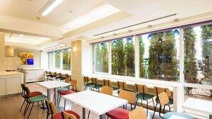 Un vaste espace de restauration intérieur, doté de nombreuses tables et chaises, et de grandes fenêtres offrant une vue sur les arbres et un bâtiment à l’extérieur.