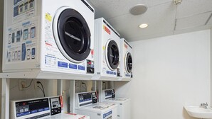 Une rangée de machines à laver à chargement frontal dans un espace commercial, avec les panneaux de commande et les consignes de sécurité bien visibles.