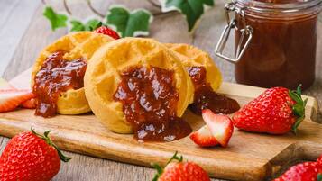 Waffles com geleia e morangos sobre uma tábua de madeira.