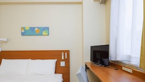 Une chambre d’hôtel comprenant un lit, un bureau avec une télévision, une prise de courant et un tableau accroché au mur.