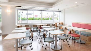 A modern dining area with multiple tables and chairs, large windows with a view of the street, and a red cushioned bench.