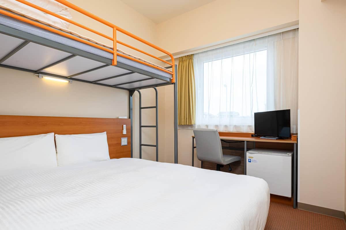 Una habitación de hotel con literas, un escritorio con computadora y una ventana con cortinas.