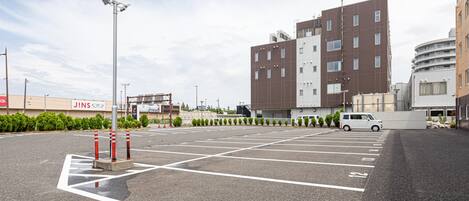 Um parque de estacionamento com vagas demarcadas, uma carrinha branca e um edifício com vários andares e janelas.