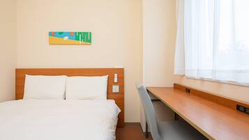 A hotel room with a bed, a desk, and a window with white curtains.