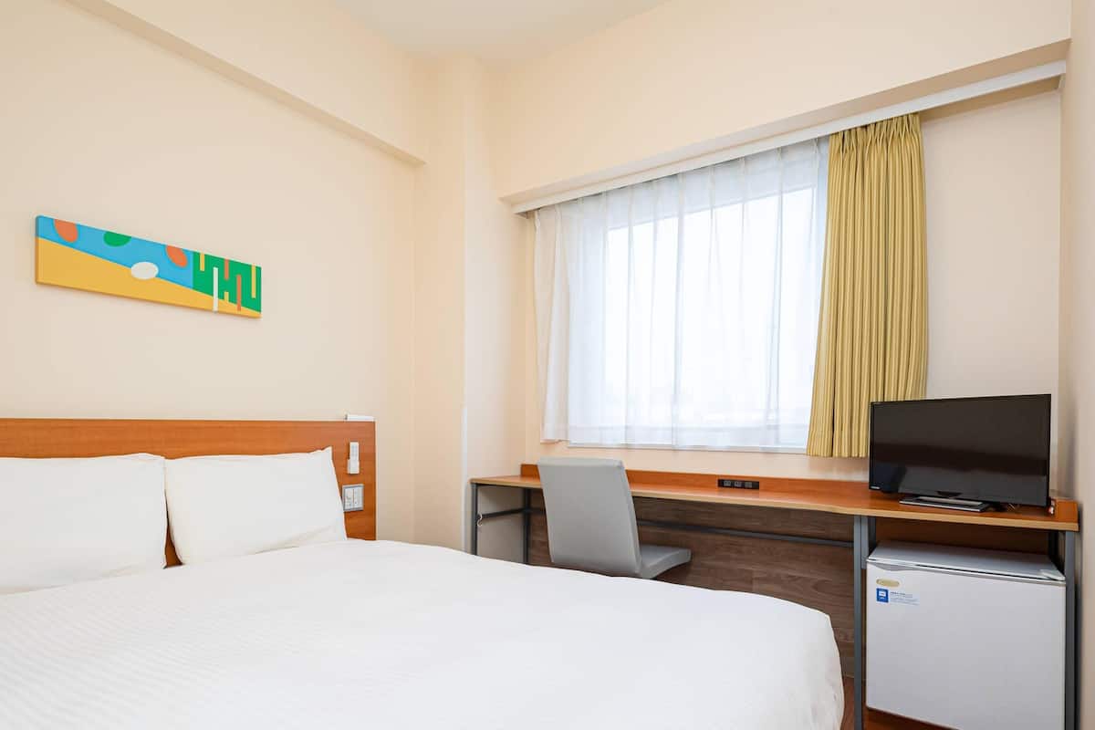 Habitación de hotel con cama, escritorio, televisión y refrigerador pequeño.