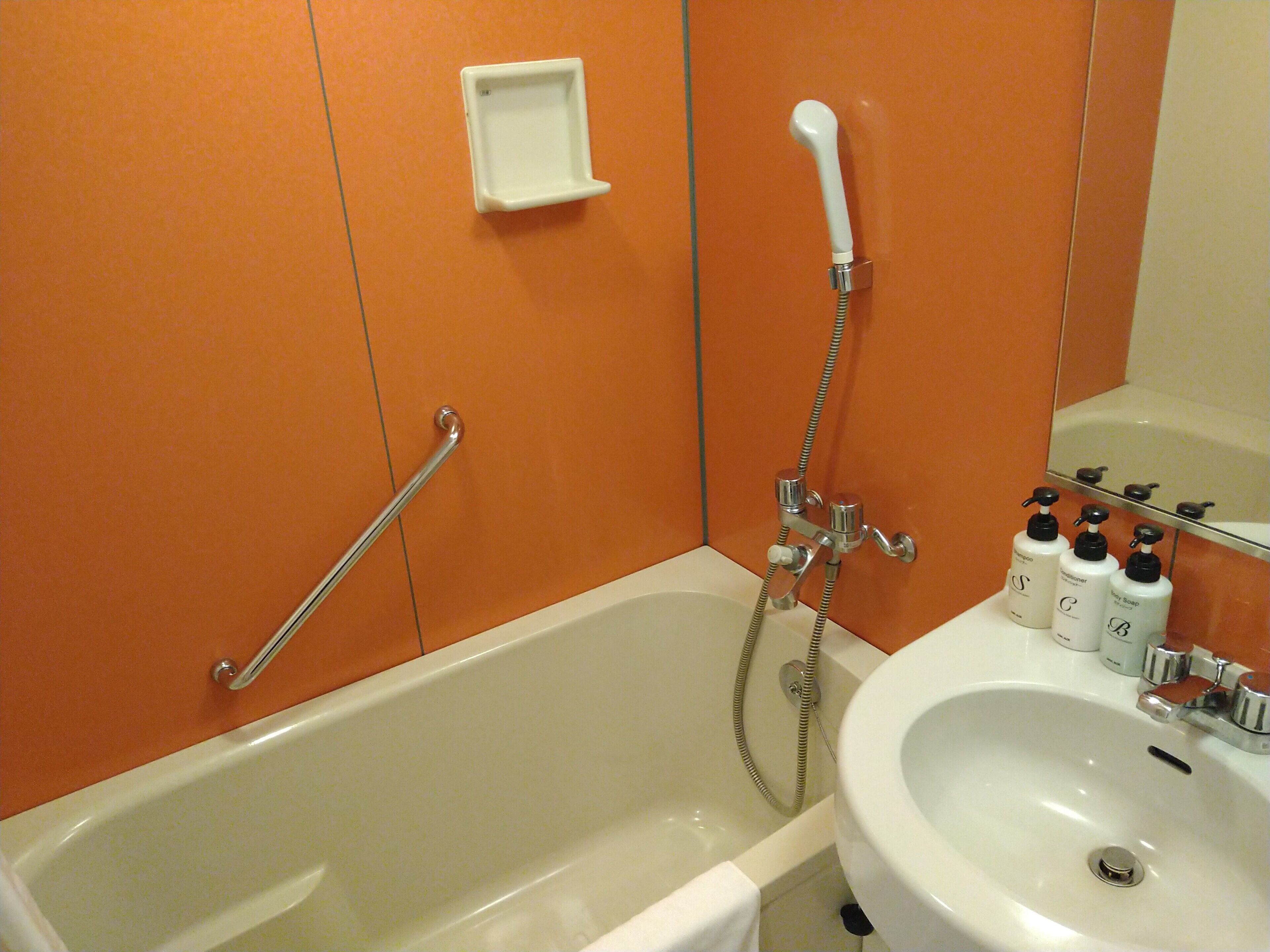 A bathroom with a bathtub, a shower, a sink, and hand soap bottles.