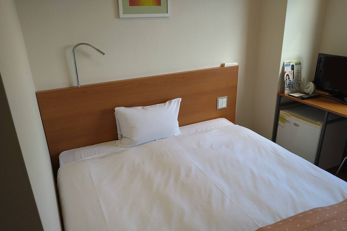 Ein Hotelzimmer mit Bett, Nachttisch, Schreibtisch, Fernseher und Wanduhr.