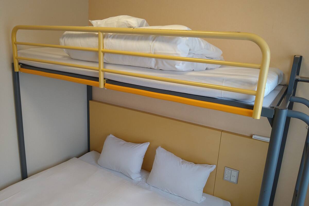 Ein Etagenbett mit zwei Schlafstellen, jeweils mit weißer Bettwäsche und Kissen.