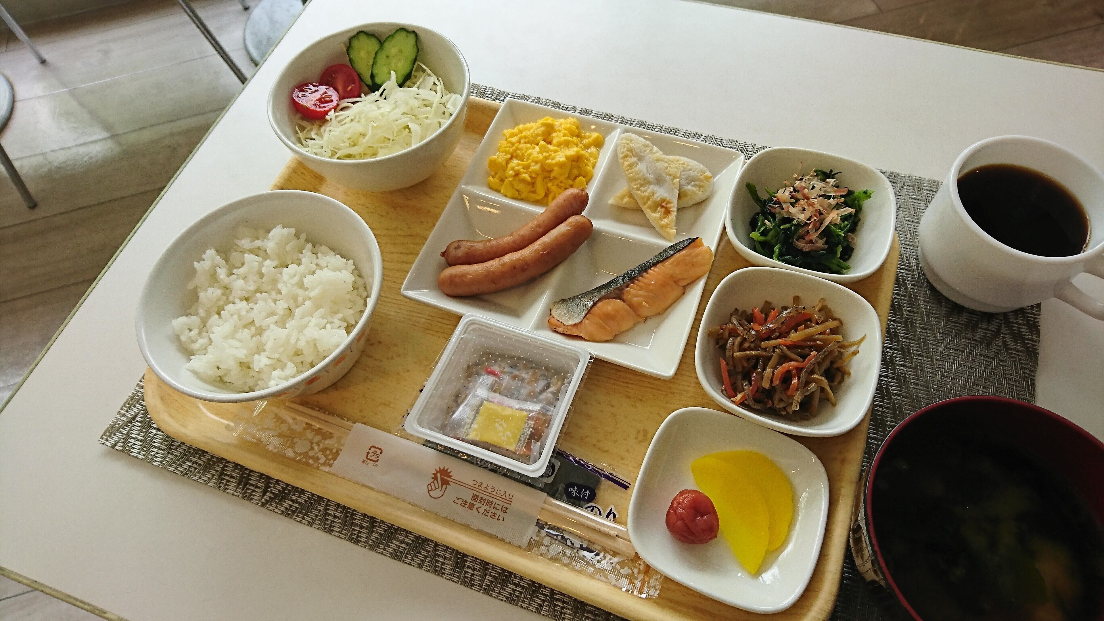 Bandeja de comida con arroz, salchichas, huevos, verduras y una taza de café.