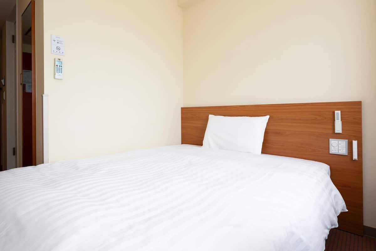 A hotel room with a wooden headboard, a white bedspread, and a control panel on the wall.